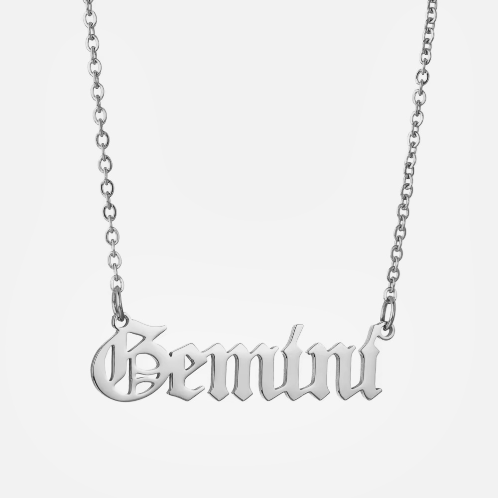 A silver stainless steel necklace with the word 'Gemini' inscribed in a gothic font on a chain with a 2-inch extender.