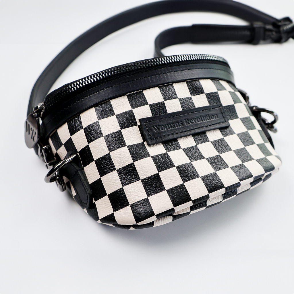 A black and white checkered Amara Petite Bum Bag with a zipper closure, a shoulder strap, and the brand 'Womxn's Revolution' visible on the front.