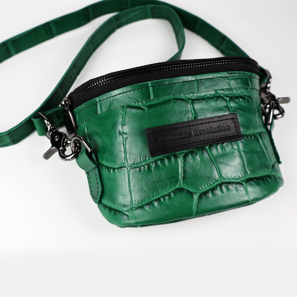A green crocodile press leather Amara Petite Bum Bag with a zipper closure, a shoulder strap, and the brand 'Womxn's Revolution' visible on the front.