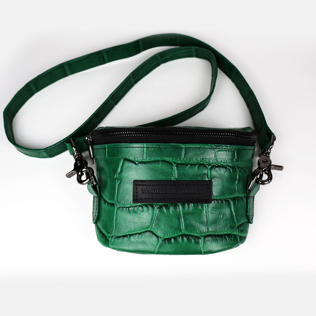 A green crocodile press leather Amara Petite Bum Bag with a zipper closure, a shoulder strap, and the brand 'Womxn's Revolution' visible on the front.