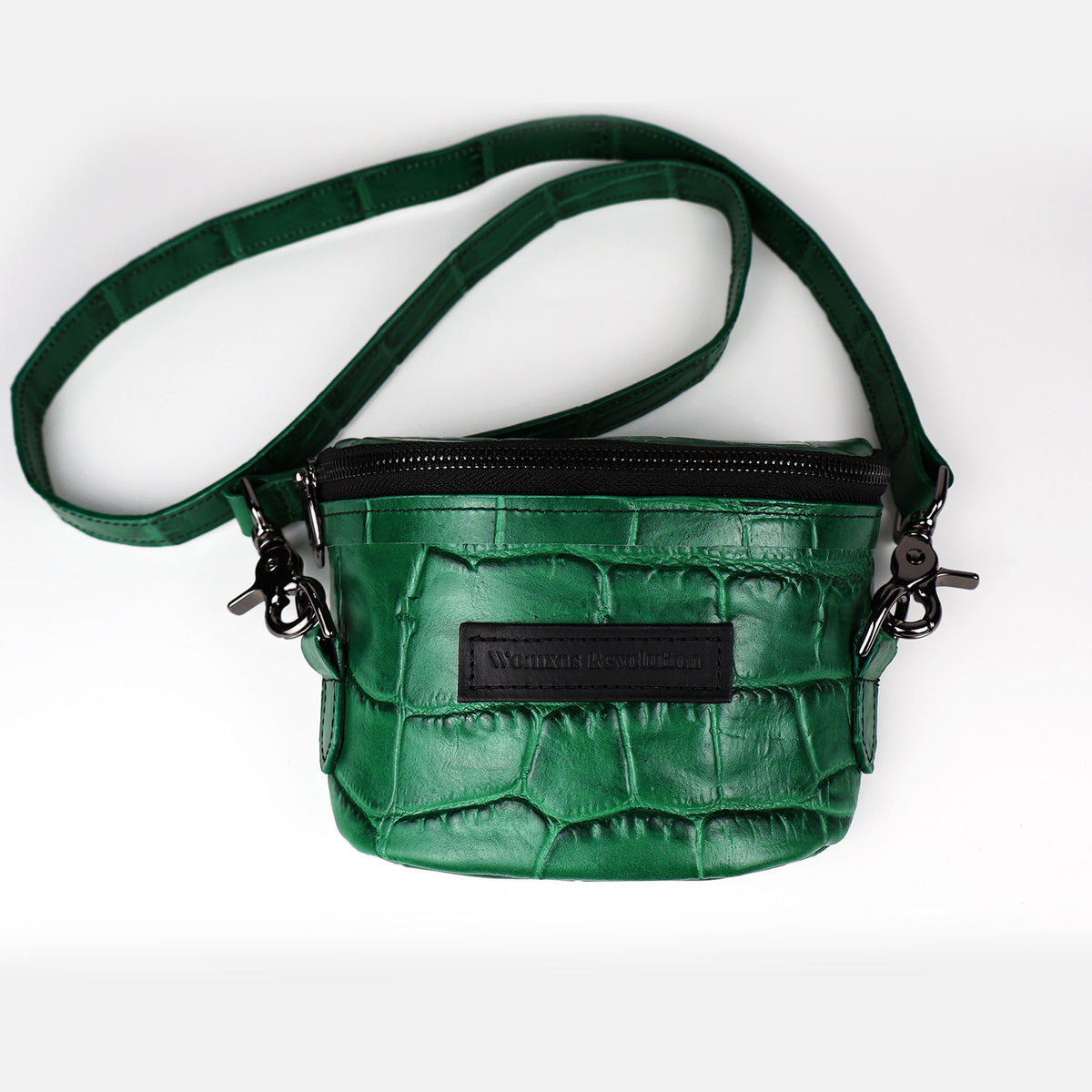 A green crocodile press leather Amara Petite Bum Bag with a zipper closure, a shoulder strap, and the brand 'Womxn's Revolution' visible on the front.