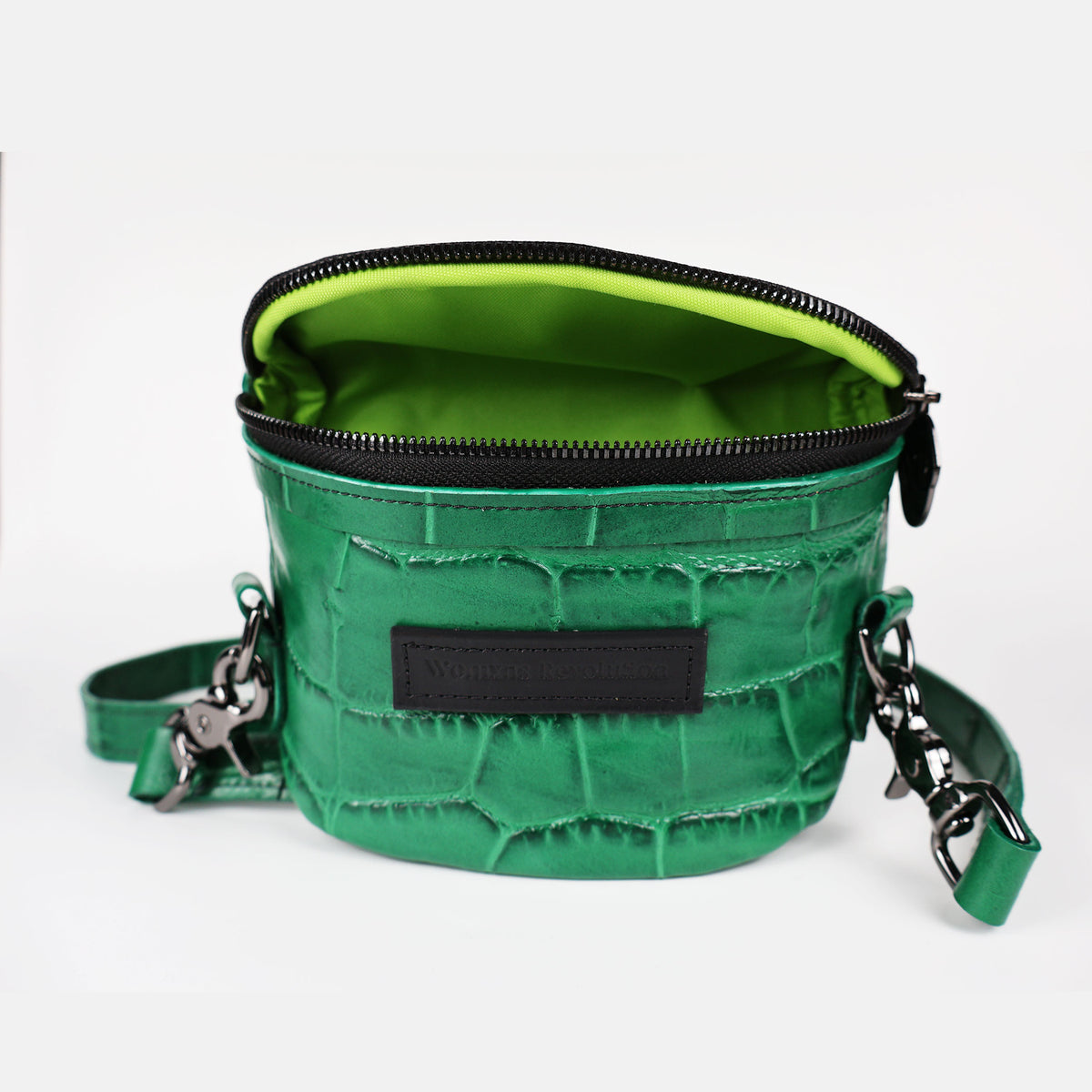 A green crocodile press leather Amara Petite Bum Bag with a zipper closure, a shoulder strap, and the brand 'Womxn's Revolution' visible on the front.