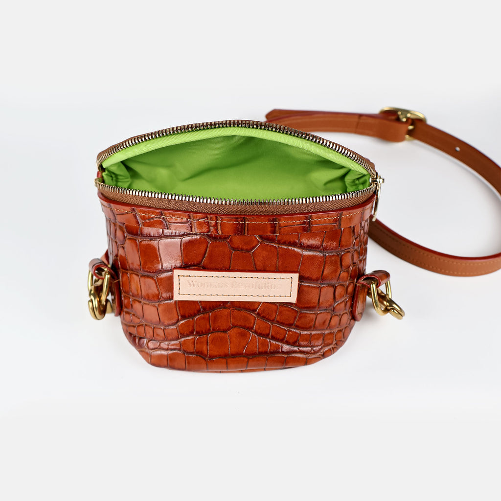 Small brown croc-embossed leather crossbody bum bag with gold zipper and hardware, open to reveal a vibrant green lining, on a white studio background