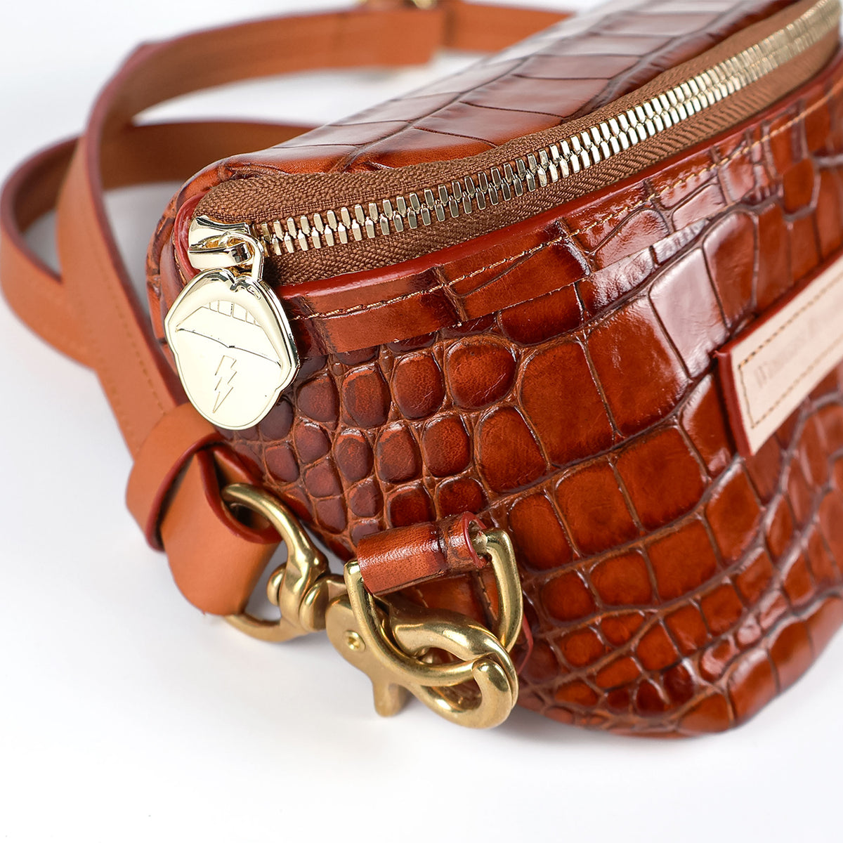 Detailed view of brown croc-embossed leather bum bag with gold zipper, lightning-shaped zipper charm, and adjustable leather strap.
