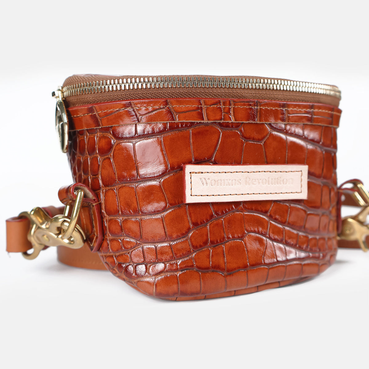 Close-up detail of a brown croc-embossed leather petite bum bag featuring gold zipper, lightning bolt zipper pull, brass hardware, and adjustable leather strap on a white background.