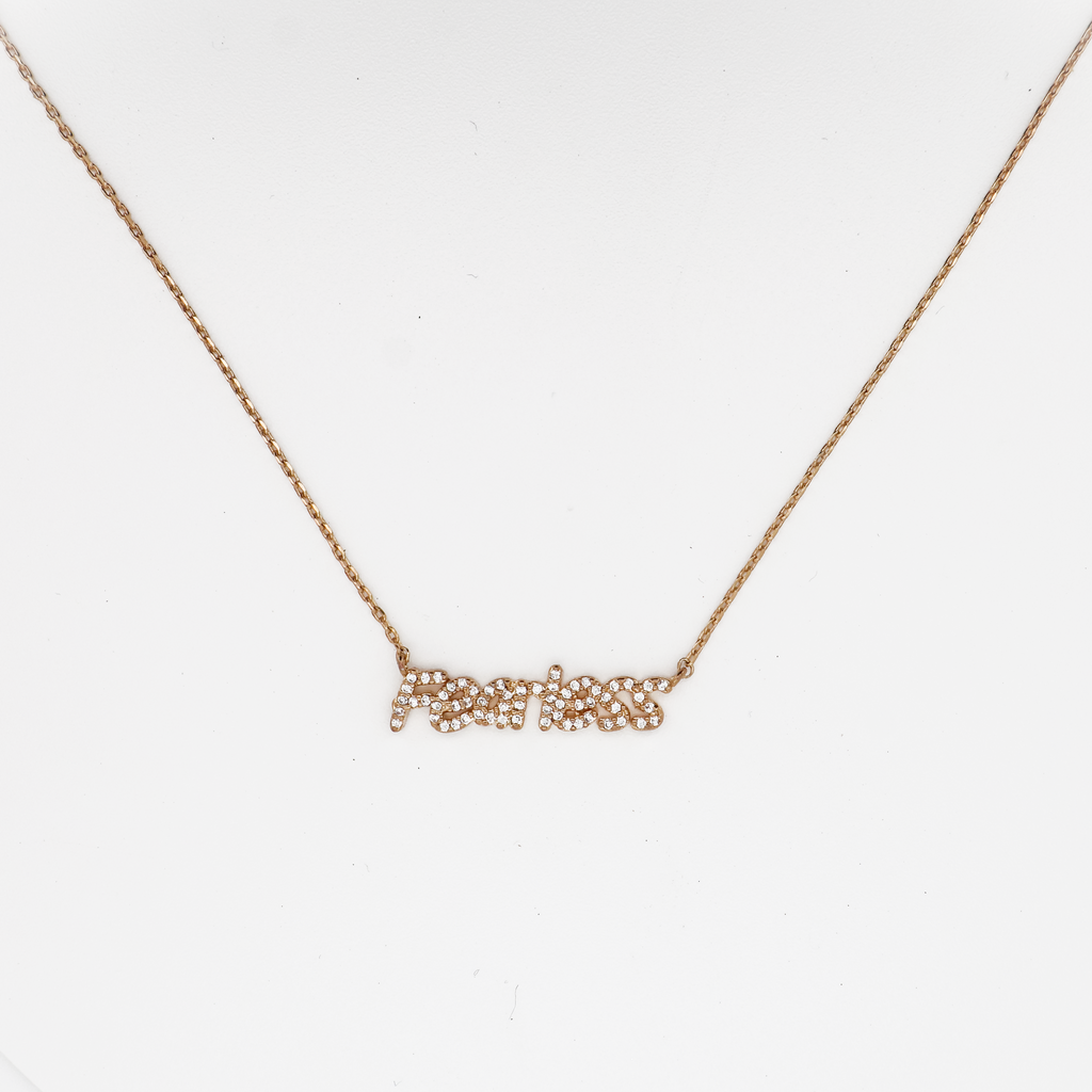 Gold ‘Fearless’ nameplate necklace with crystal accents on a delicate chain, photographed on a white background