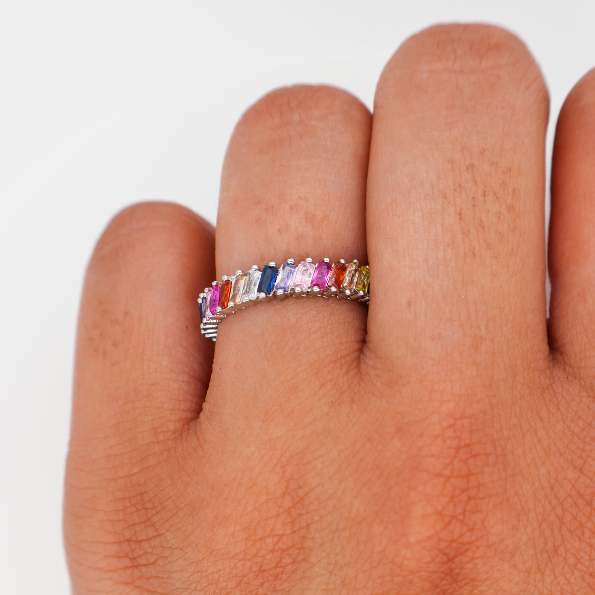 Silver band ring set with multicolor baguette-cut crystals, worn on a finger against a white background.